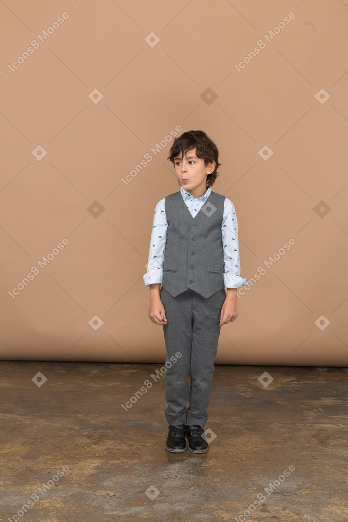 Vista frontal de um menino fofo em um terno cinza olhando para o lado