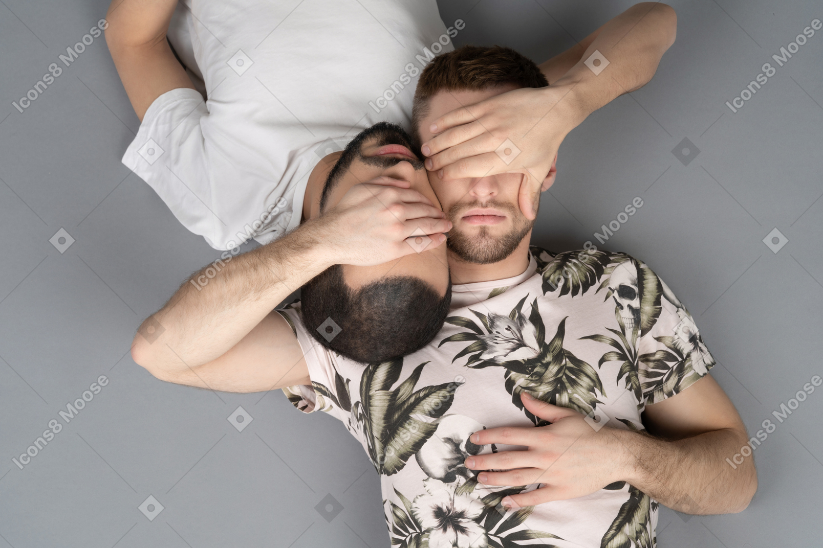 Distesa piatta di due giovani uomini caucasici sdraiati simmetricamente testa a testa chiudendosi gli occhi con le mani