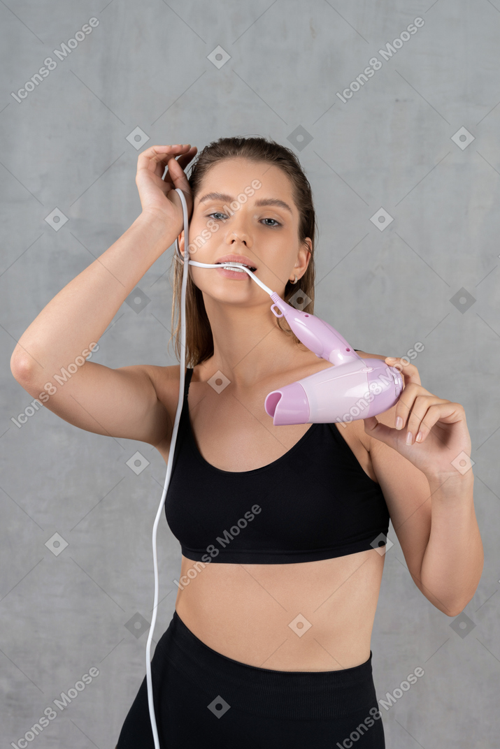 Young woman touching forehead while biting on hairdryer cord