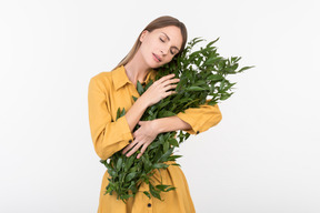Young woman hugging green twigs with eyes closed