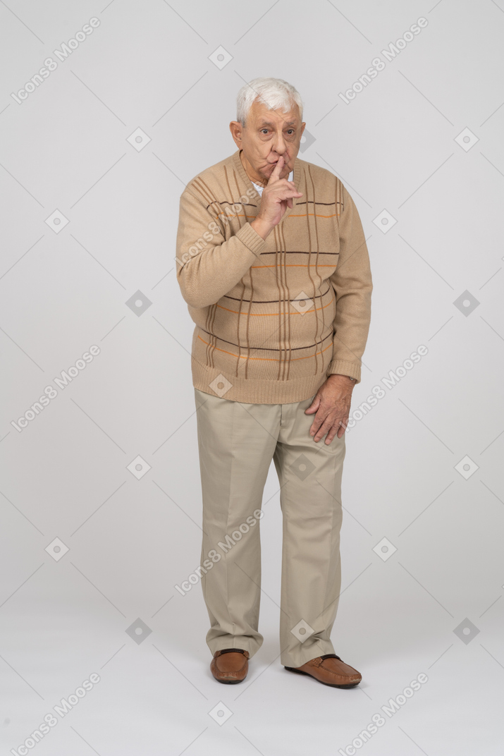 Front view of an old man in casual clothes making shhh gesture
