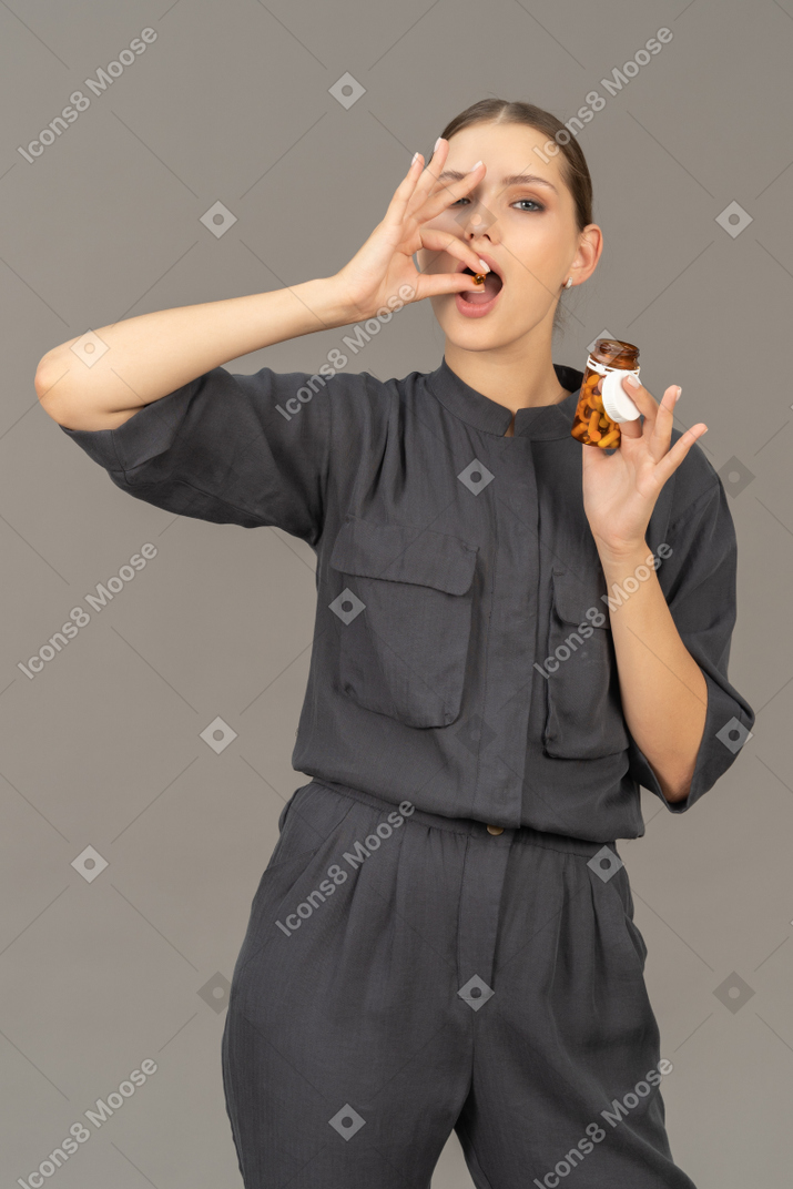 一名身穿连衣裤的年轻女子从罐子里取出药丸的前视图