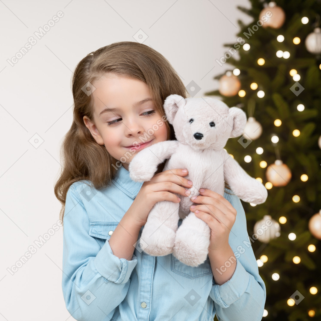 Linda niña sosteniendo su oso de juguete cerca del árbol de navidad