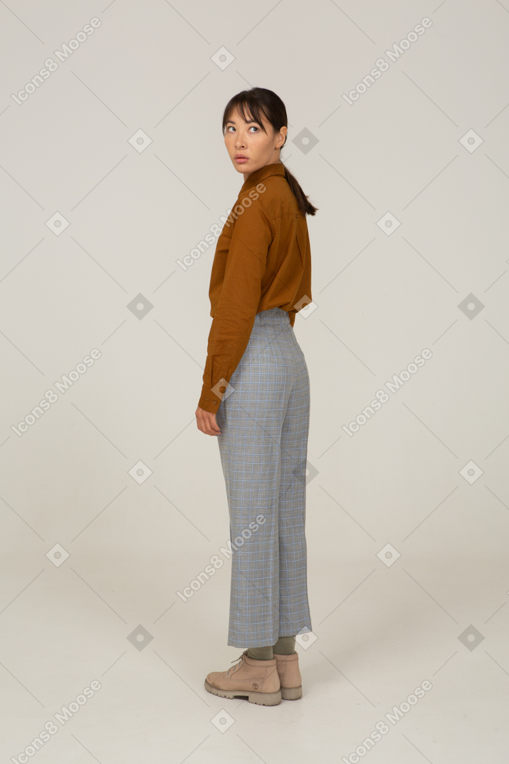 Vista traseira a três quartos de uma jovem mulher asiática de calça e blusa, virando-se