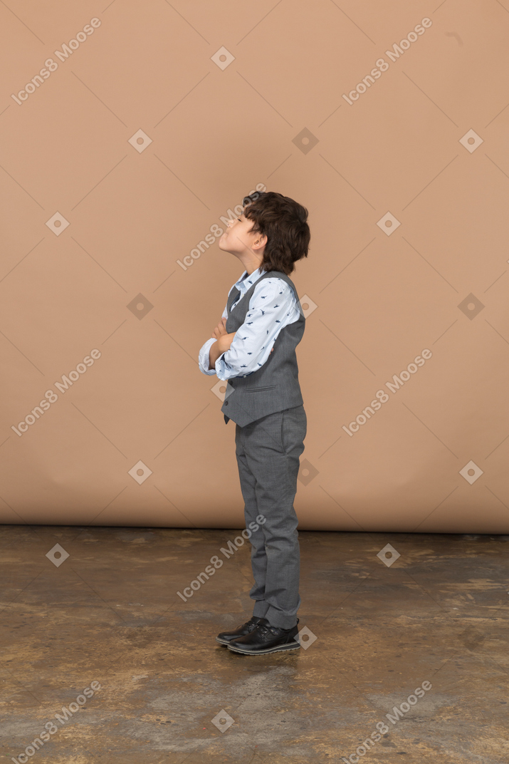 自分を抱き締める灰色のスーツを着た少年の側面図