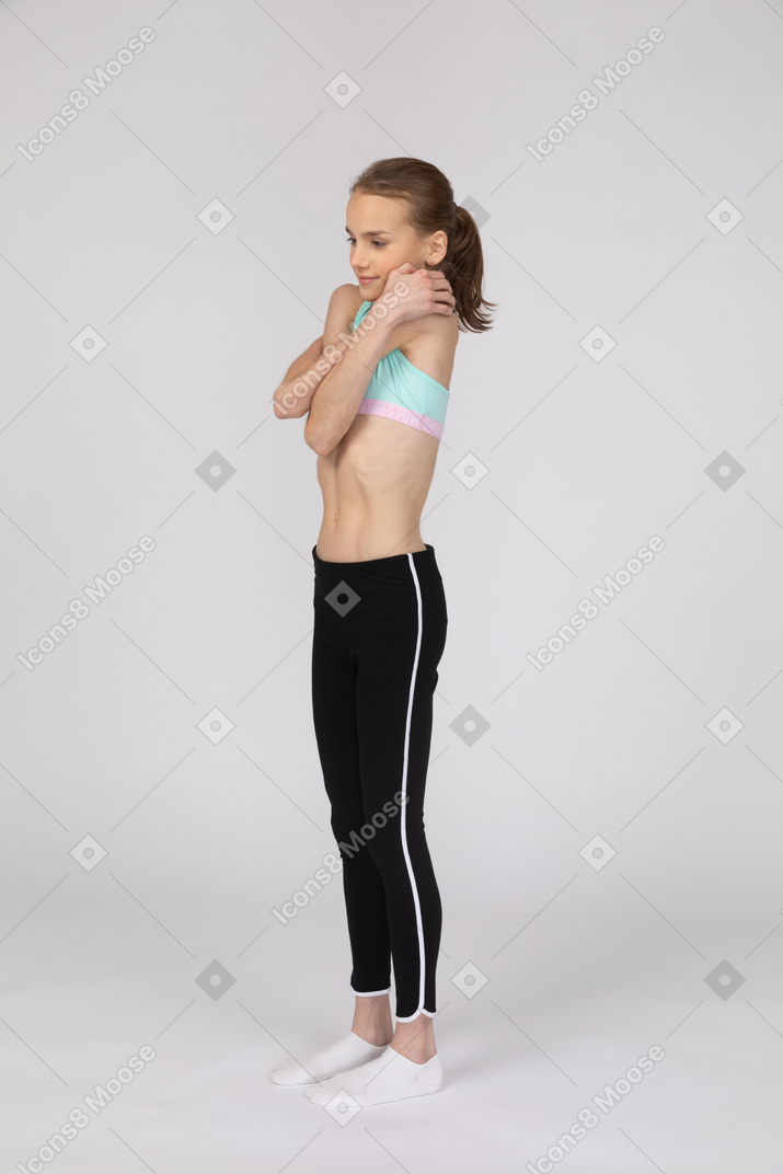Three-quarter view of a teen girl in sportswear embracing herself