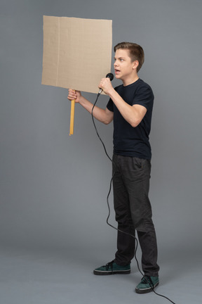 Молодой человек говорит в микрофон и держит плакат