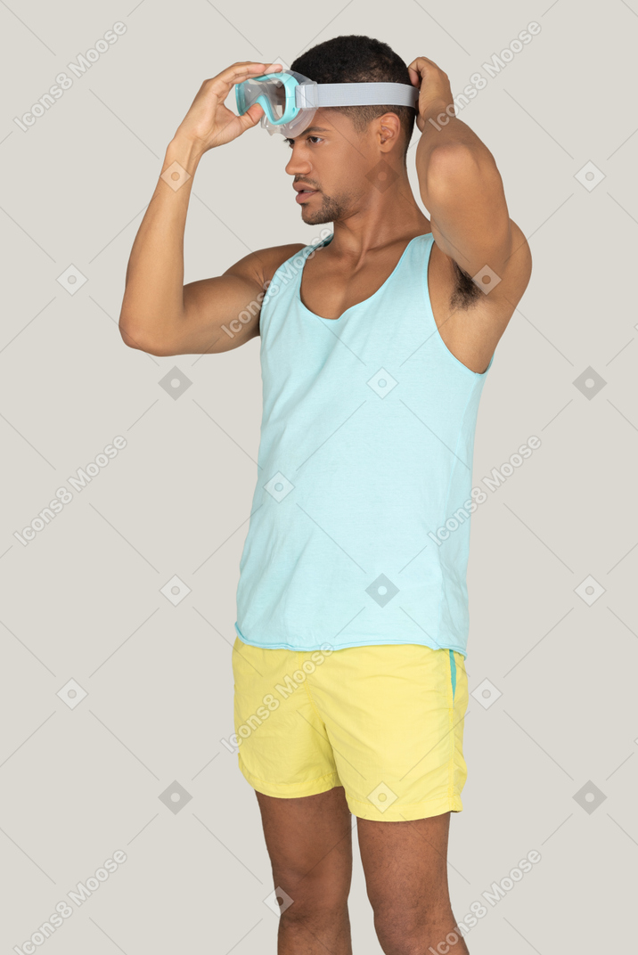 A man in a blue tank top putting on goggles