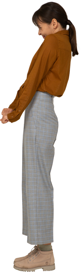 Vista lateral de uma jovem mulher asiática de calça e blusa de mãos dadas e inclinada para trás