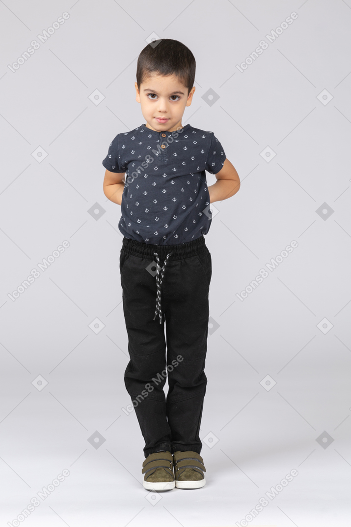 Front view of a cute boy standing with hands on back and looking at camera
