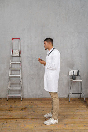 Vista lateral de un joven médico de pie en una habitación con escalera y silla explicando algo