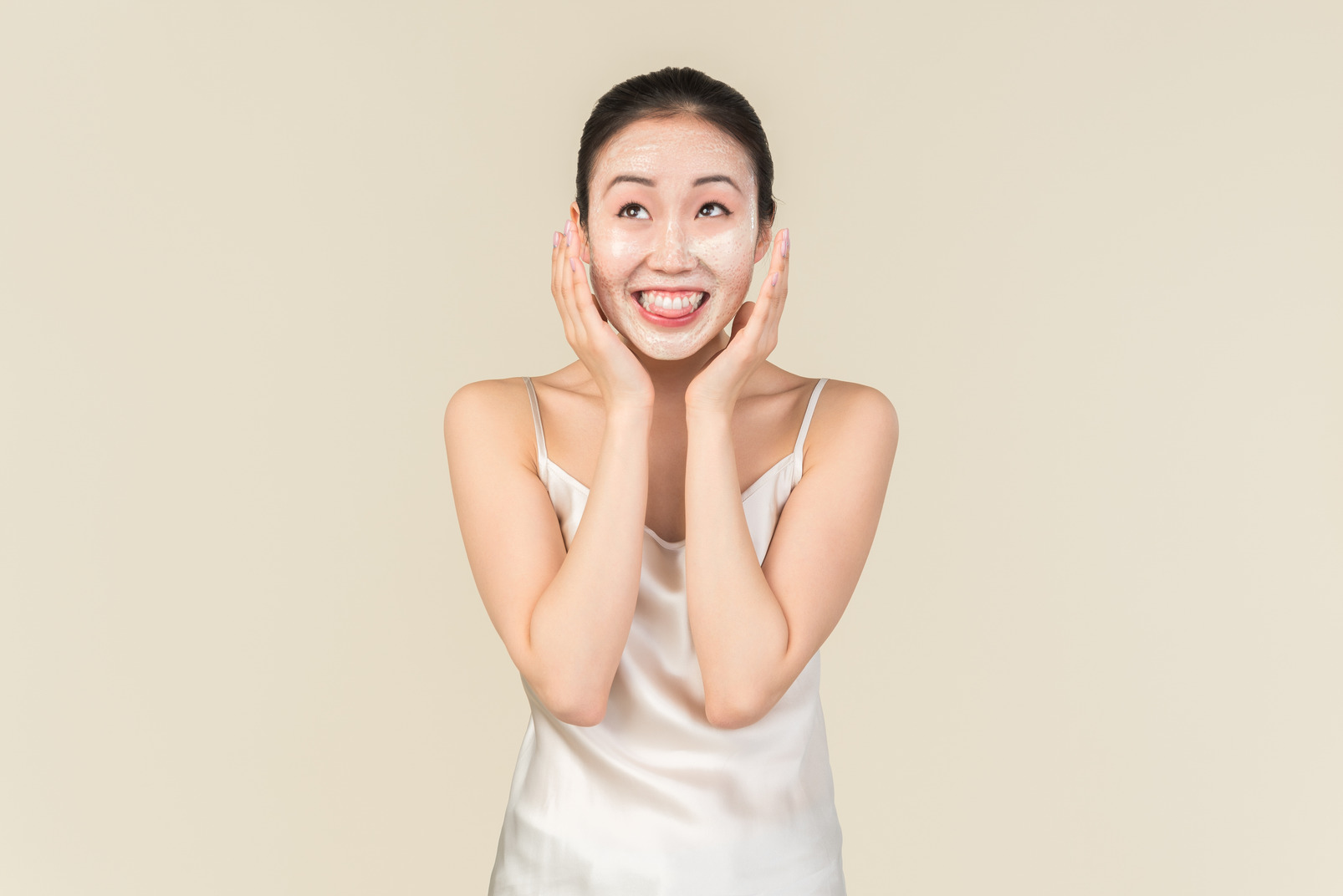 Smiling young asian woman with facial mask on touching face