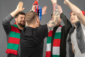 Close-up of four happy male football fans giving high five