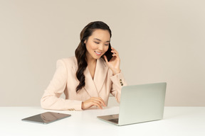 Asiatischer weiblicher büroangestellter, der am telefon spricht und an laptop arbeitet