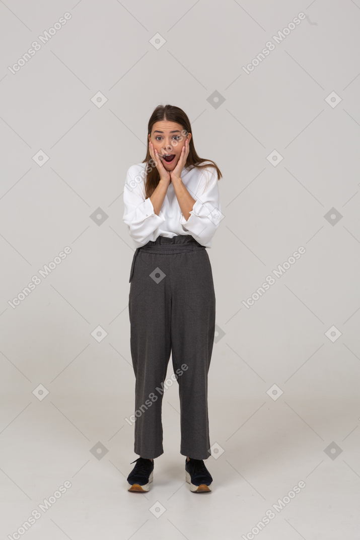 Front view of an excited young lady in office clothing touching face