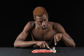 Front view of a young afro man cutting meat