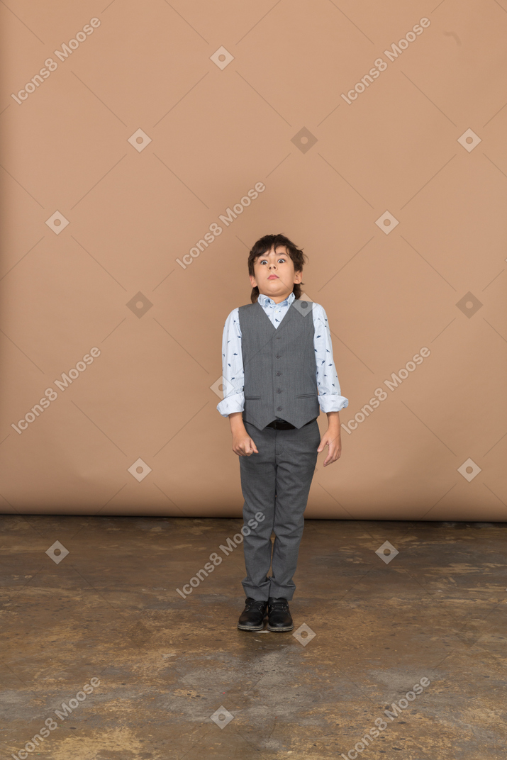 Vista frontal de un niño asustado en traje mirando a la cámara