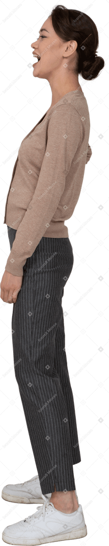 Vista lateral de una mujer riendo en jersey y pantalones poniendo la mano en la cadera