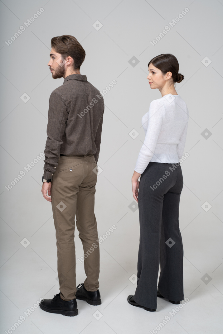 Vista traseira de três quartos de um jovem casal com roupas de escritório, parado