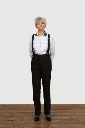 Front view of an old funny female in office clothes grimacing with her hands behind back