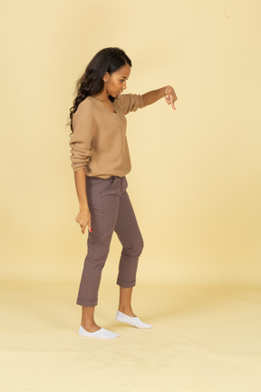 Vista lateral de una mujer joven de piel oscura que señala con el dedo hacia abajo