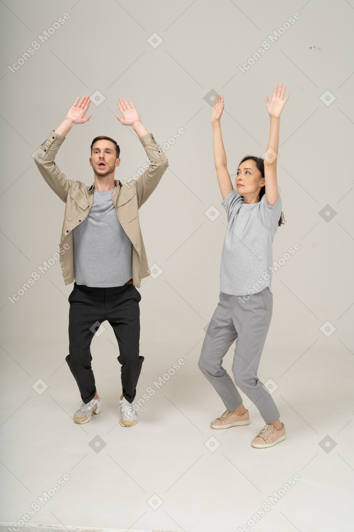 Young man and woman bending legs and raising hands