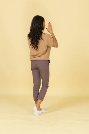 Three-quarter back view of a dark-skinned young female holding hands near her face