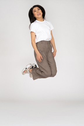 Vista frontal de uma jovem saltitante de calça e camiseta dobrando os joelhos