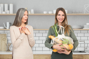 A shocked woman standing next to a woman holding reusable bag with groceries