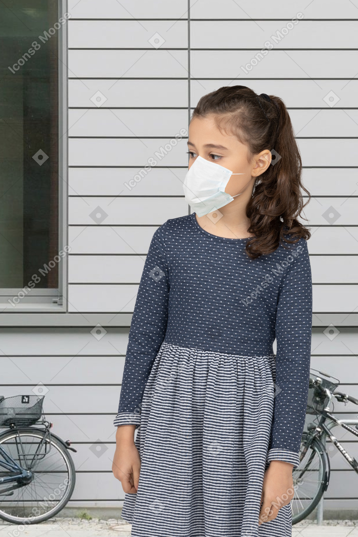A young girl wearing a face mask standing in front of a house