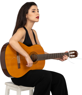 Vista de tres cuartos de una joven sentada en traje negro sosteniendo la guitarra