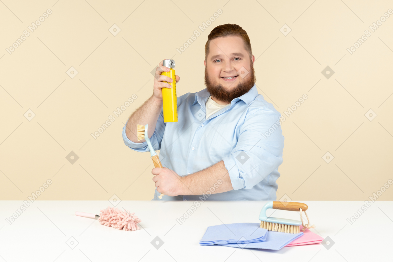 Contented young overweight man sitting at the table and holding cleaning equipment