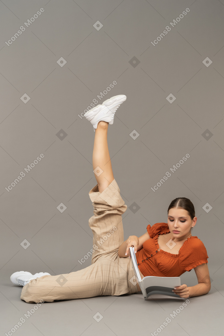 Young woman stretching her leg while reading a book