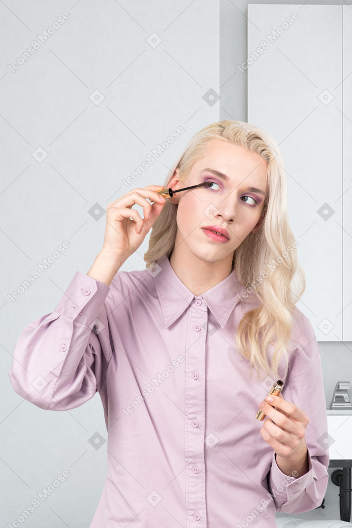 A woman in a pink shirt is putting on mascara