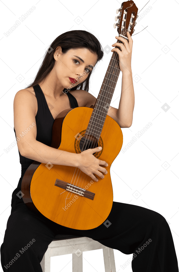 Vista frontal de una señorita sentada en traje negro abrazando su guitarra