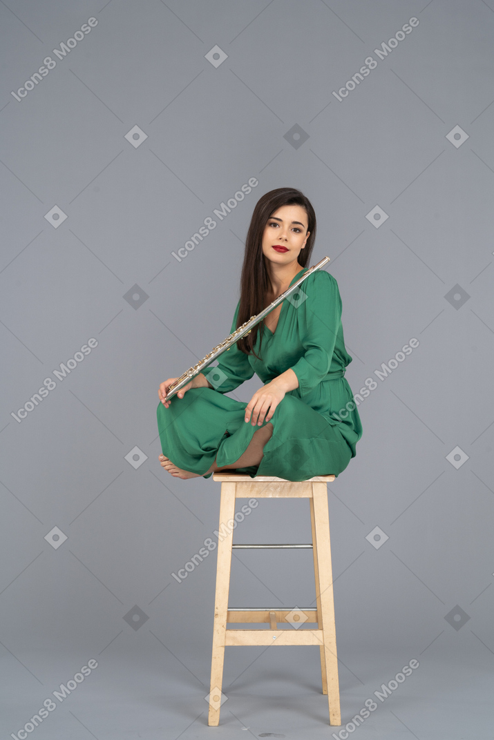 Full-length of a young lady holding the clarinet sitting with her legs crossed on a wooden chair