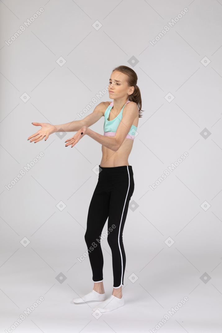 Вид в три четверти на недовольную девушку-подростка в спортивной одежде, протягивающую руки