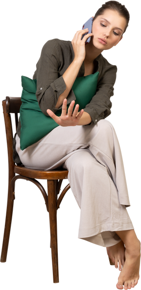 Vista frontal de una mujer joven sentada en una silla mientras tiene una llamada telefónica