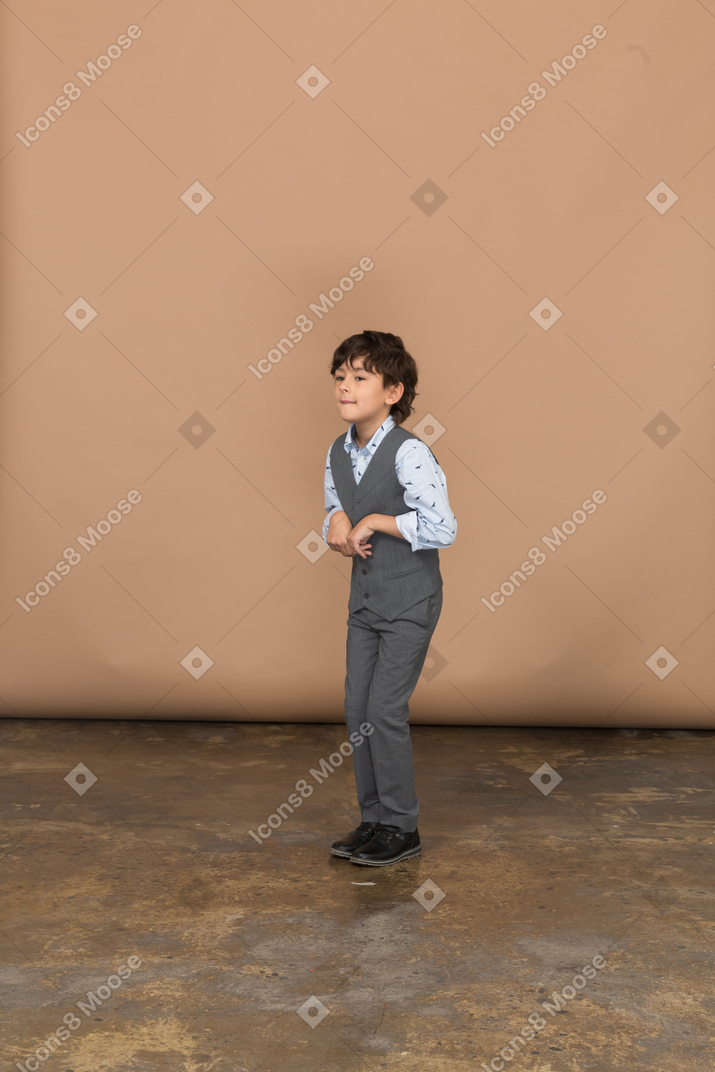 Vista frontal de un chico lindo en traje gris mirando a la cámara