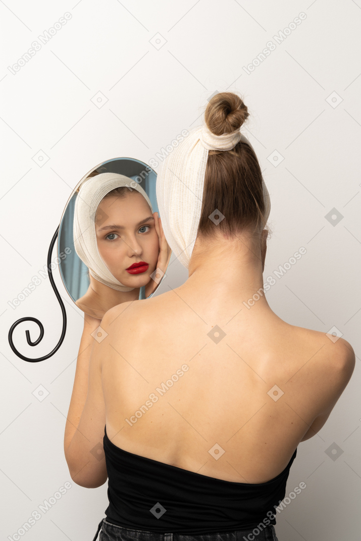 Jeune femme avec un bandage de tête regardant dans le miroir
