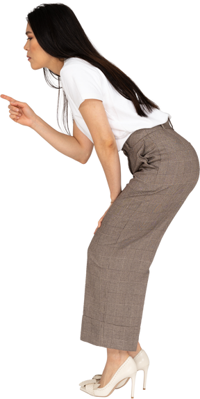 Vista laterale di una rigorosa giovane donna in calzoni e t-shirt chinandosi