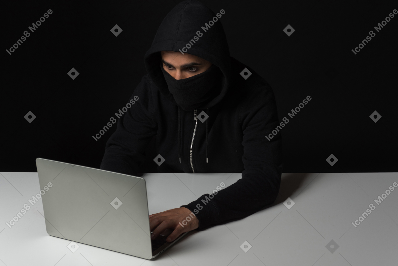 Hacker guy sitting at the table and working on laptop in the dark