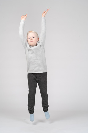 Vista frontal de um menino pulando com as mãos levantadas