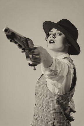 Femme confiante au chapeau visant le pistolet avec une main
