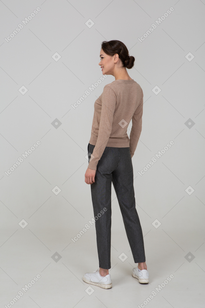 一个微笑的女性，在套头衫和裤子的四分之三后视图
