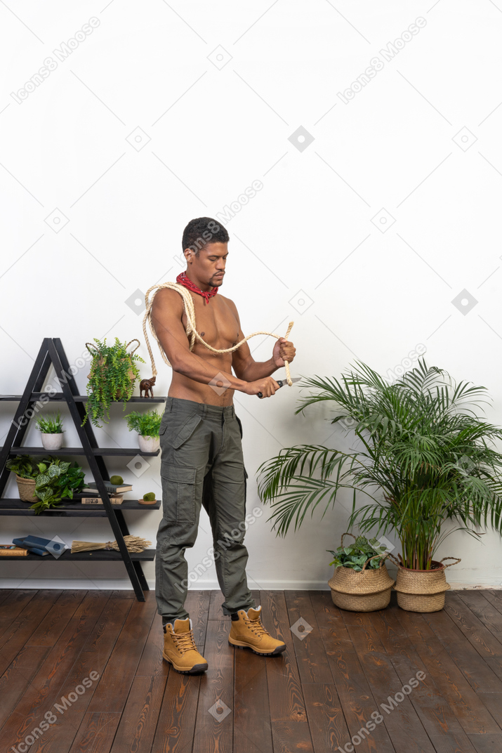 Athletic man standing and using a knife to cut rope