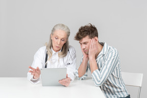 Alter weiblicher doktor, der einem patienten etwas auf ihrer digitalen tablette zeigt