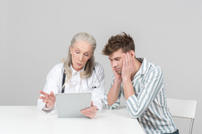 Aged female doctor showing something on her digital tablet to a patient