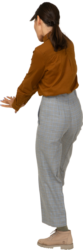 Vista traseira a três quartos de uma jovem mulher asiática de calça e blusa estendendo as mãos