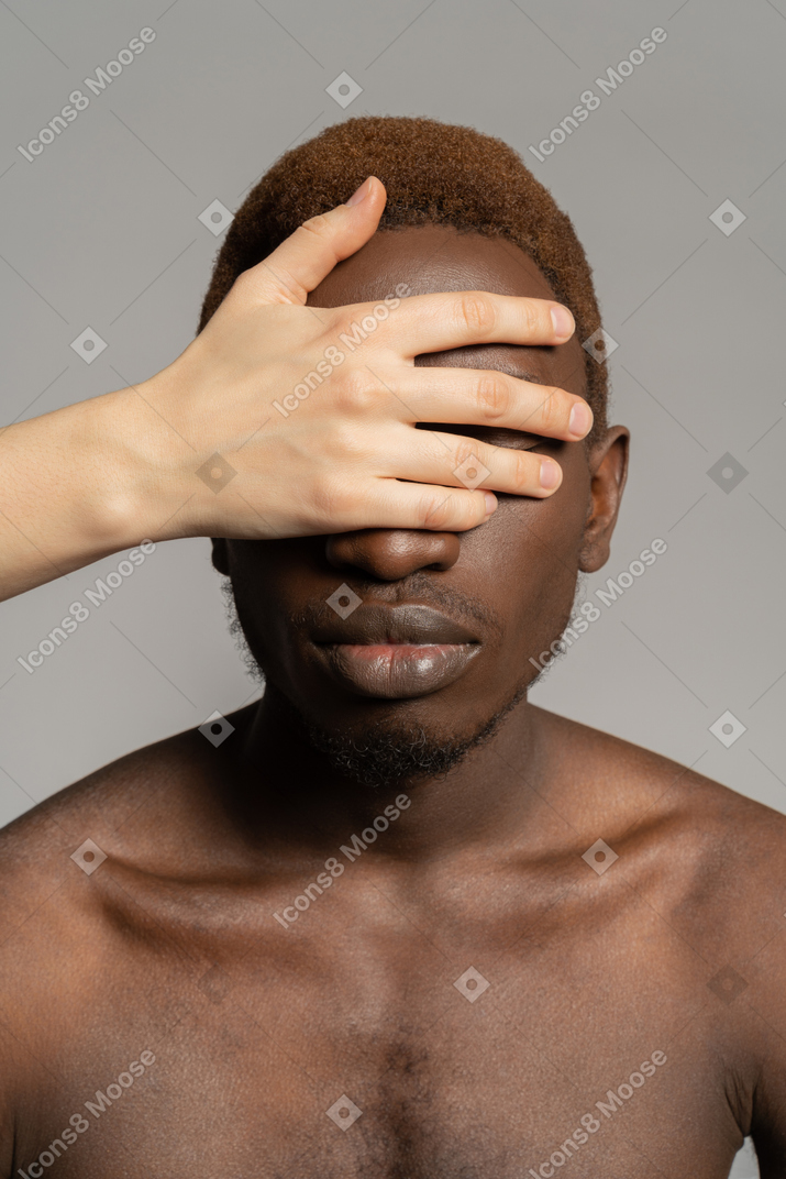 White hand covering eyes of a black young man